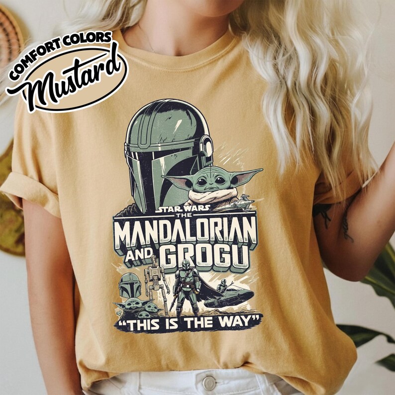 Puede incluir: Camiseta de color mostaza con un gr&aacute;fico de Star Wars de The Mandalorian y Grogu. El dise&ntilde;o incluye el casco del Mandaloriano, Grogu y la frase "THIS IS THE WAY". La camiseta tambi&eacute;n tiene las palabras "COMFORT COLORS" y "Mustard".