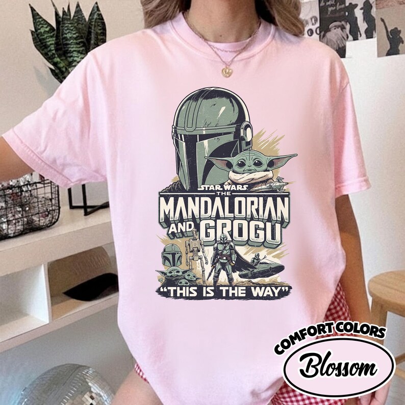 Puede incluir: Camiseta Comfort Colors rosa p&aacute;lido con un dise&ntilde;o de Star Wars que presenta a The Mandalorian y Grogu. El gr&aacute;fico incluye el casco del Mandaloriano, Grogu y la frase "THIS IS THE WAY". La camiseta est&aacute; etiquetada como "Blossom".