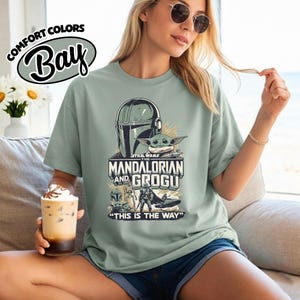 Puede incluir: Camiseta verde salvia con un dise&ntilde;o de Star Wars con The Mandalorian y Grogu. El gr&aacute;fico incluye el casco del Mandaloriano, Grogu y la frase "THIS IS THE WAY". La camiseta tambi&eacute;n tiene el logo Comfort Colors Bay.
