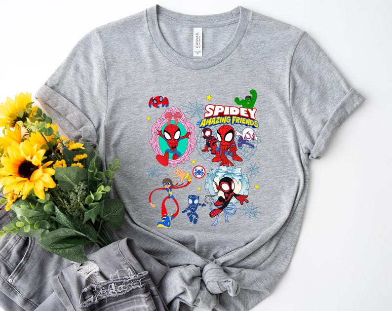 May include: A gray t-shirt featuring the text "Spidey and His Amazing Friends" with cartoon illustrations of Spider-Man and other characters. The design includes various colorful elements and is printed on a soft, casual tee.