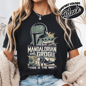Puede incluir: Camiseta negra con un gr&aacute;fico de Star Wars que presenta a The Mandalorian y Grogu. El dise&ntilde;o incluye el casco del Mandaloriano, Grogu y la frase "THIS IS THE WAY". La camiseta tambi&eacute;n tiene el texto "COMFORT COLORS Black".