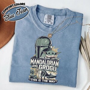 Puede incluir: Una camiseta azul Comfort Colors con un gr&aacute;fico de The Mandalorian y Grogu de Star Wars. El dise&ntilde;o incluye un casco, Grogu y el texto "THIS IS THE WAY". La camiseta tiene cuello redondo y mangas cortas.