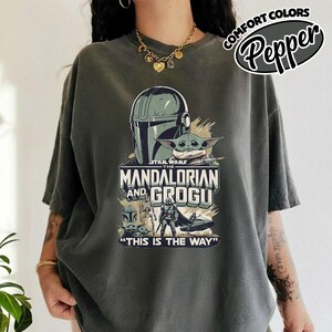 Puede incluir: Camiseta gris oscuro con un gr&aacute;fico de la serie Star Wars, "The Mandalorian and Grogu". El dise&ntilde;o incluye el casco del Mandaloriano, Grogu y la frase "This is the Way". La camiseta tambi&eacute;n tiene el texto "Comfort Colors" y "Pepper".