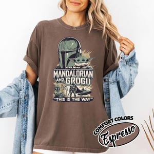 Puede incluir: Camiseta color espresso con un gr&aacute;fico de The Mandalorian y Grogu de Star Wars. El dise&ntilde;o incluye el casco del Mandaloriano, Grogu y el texto "THIS IS THE WAY". La camiseta es parte de la colecci&oacute;n Comfort Colors.