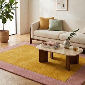 May include: A living room scene featuring a mustard yellow and pink rug, a cream-colored sofa with mustard and green pillows, and a marble coffee table. A potted plant and artwork complete the cozy, modern aesthetic.