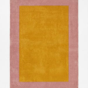 May include: A rectangular area rug featuring a solid mustard yellow centre panel surrounded by a wide, solid dusty rose pink border. The rug has a uniform, short-pile texture throughout, creating a clean, geometric design with two distinct colour blocks.