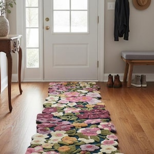 Puede incluir: Una alfombra larga con estampado floral en un pasillo. La alfombra presenta un fondo azul oscuro con grandes flores de color rosa, blanco, amarillo y verde. La alfombra está colocada sobre un suelo de madera.