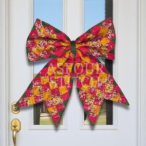 May include: A large decorative bow featuring a patchwork design of pink floral fabric and solid yellow squares, accented with green fabric edges. The bow is centered on a white door and displays the text ASFOUR STITCH in white lettering.