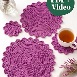 May include: Two large round purple crochet doilies and two smaller matching crochet coasters with scalloped edges. A green circular graphic with the white text PDF + Video is overlaid on the image. The items are arranged with a white teacup.