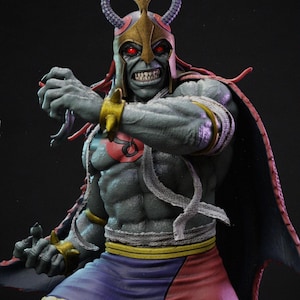 May include: A grey-skinned humanoid figurine with red eyes, wearing a gold helmet topped with two snake heads, a gold spiked wristband, a red circular chest emblem, a purple and red skirt, and a dark cape with a red interior lining.