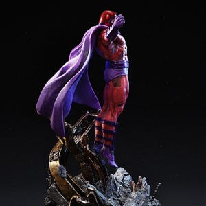 Op de afbeelding: Gedetailleerd beeldje van een superheld in een dynamische pose. Het figuur is gekleed in een rood en paars pak met bijpassende helm en cape. De basis is een gedetailleerde, rotsachtige structuur met metalen accenten.