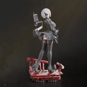 May include: A collectible figurine of a character with short white hair, wearing a black dress with intricate silver embroidery, black thigh-high boots, and a blindfold. A mechanical arm with a rectangular device extends from the back.