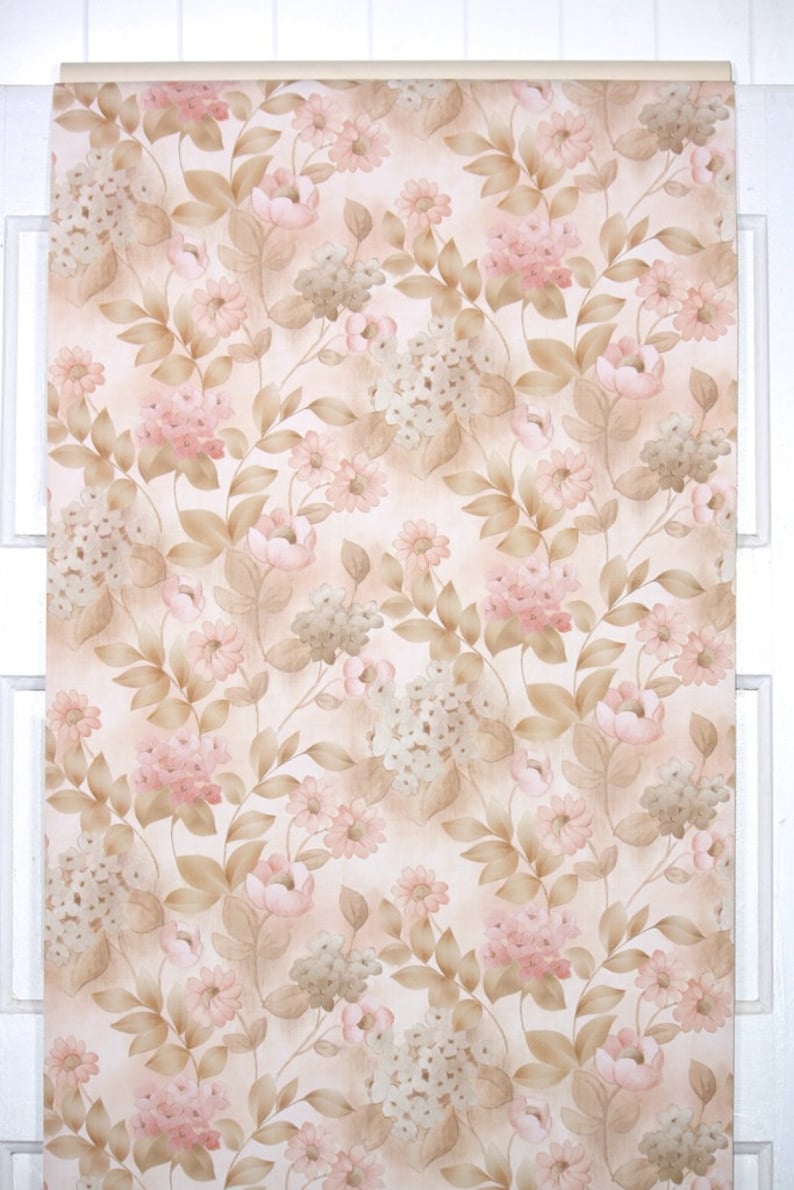 Puede incluir: Un rollo de papel pintado vintage con un patr&oacute;n floral repetitivo. El dise&ntilde;o incluye flores rosas y blancas, hojas y tallos marrones, sobre un fondo beige claro. El papel pintado se muestra contra un marco de ventana blanco.