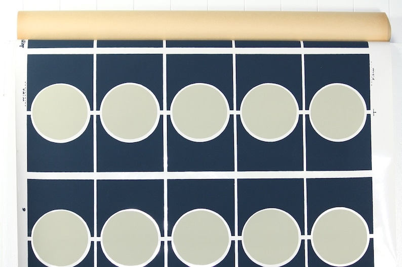 May include: Wallpaper roll with a repeating pattern of light grey circles within navy blue squares, connected by white lines. The roll is beige and is at the top. The design is modern and geometric, suitable for interior decoration.