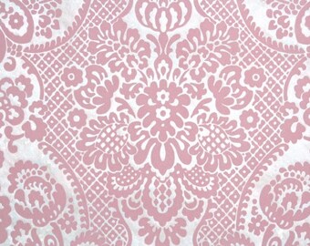 May include: A close-up of a pink and white damask pattern. The design features a repeating floral and scroll motif, creating a textured, ornate look. The pattern is symmetrical and suitable for wallpaper or fabric.