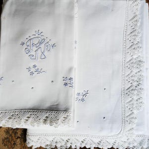 Puede incluir: Juego de ropa de cama de lino blanco con iniciales bordadas en azul y detalles florales. Los bordes están adornados con encaje blanco intrincado. Un diseño clásico y elegante.