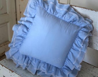 Capa de almofada azul-clara antiga com babado duplo e acabamento em renda, monograma "M.F." em relevo, estilo shabby chic/romântico.