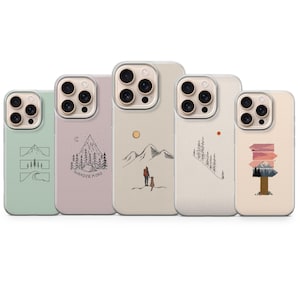 May include: A collection of five phone cases with nature-themed designs. The cases feature illustrations of mountains, trees, and a signpost, in shades of green, pink, and beige. One case has the text "Wander More".
