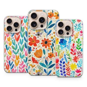 May include: Three phone cases with floral patterns. The cases display colourful flowers and leaves in different designs. The cases have a clear border and a gold-coloured camera lens area.
