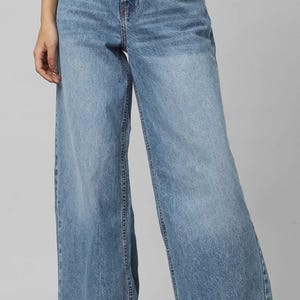 May include: Pale blue denim wide-leg jeans. The jeans feature a high waist and a classic five-pocket design. The denim has a faded wash, giving the jeans a vintage appearance. The wide leg provides a relaxed and comfortable fit. A stylish wardrobe staple.