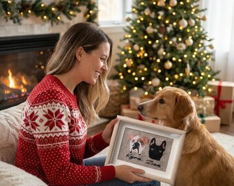 May include: A framed pet portrait featuring two dog faces, a bulldog and a black dog, with the names "Kyra Zion" below. The portrait is held by a person wearing a red sweater with a white snowflake pattern. A golden retriever sits nearby.