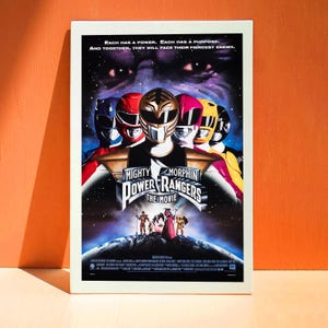 May include: A framed movie poster for "Mighty Morphin Power Rangers: The Movie." The poster shows the Power Rangers in their helmets, with the text "Each has a power. Each has a purpose. And together, they will face their fiercest enemy."