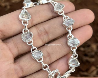 May include: A silver bracelet featuring clear, irregularly shaped gemstones. The bracelet has a toggle clasp and is composed of linked segments. The text "BhagwatiSilver925" is visible on the bracelet.