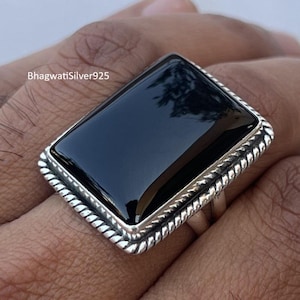 May include: A rectangular black onyx ring with a silver rope-like border. The ring is set on a silver band. The text "BhagwatiSilver925" is visible on the image.