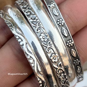 May include: A collection of silver bangles with intricate floral and scrollwork designs. The bangles vary in width and pattern, showcasing detailed craftsmanship. The image includes the text "BhagwatiSilver925".