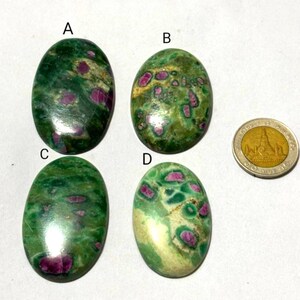 Puede incluir: Cuatro piedras preciosas ovaladas con tonos verdes y rojos. Se muestran sobre una superficie blanca, con una moneda para comparar el tamaño. Las piedras tienen una superficie pulida y un aspecto natural.