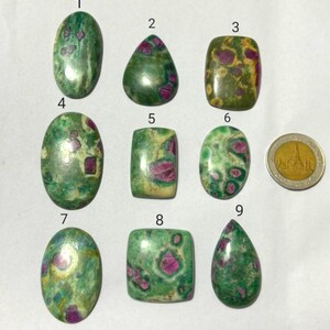 May include: A collection of nine polished gemstones in various shapes, including oval, teardrop, and rectangular. The stones feature a mottled green base color with vibrant red inclusions, and a gold coin is included for size reference.