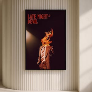 May include: A framed art print featuring a person in a suit with flames for a head. The words "LATE NIGHT DEVIL" are in red at the top. The artwork is displayed on a textured white wall.