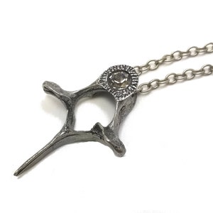May include: A silver necklace with a pendant shaped like a bone with a clear crystal in the center.
