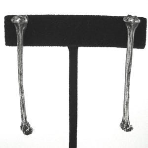May include: A pair of silver bone-shaped earrings hanging from a black display stand.