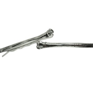 May include: Two silver hair clips shaped like bones. The clips are about 3 inches long and have a detailed bone texture.