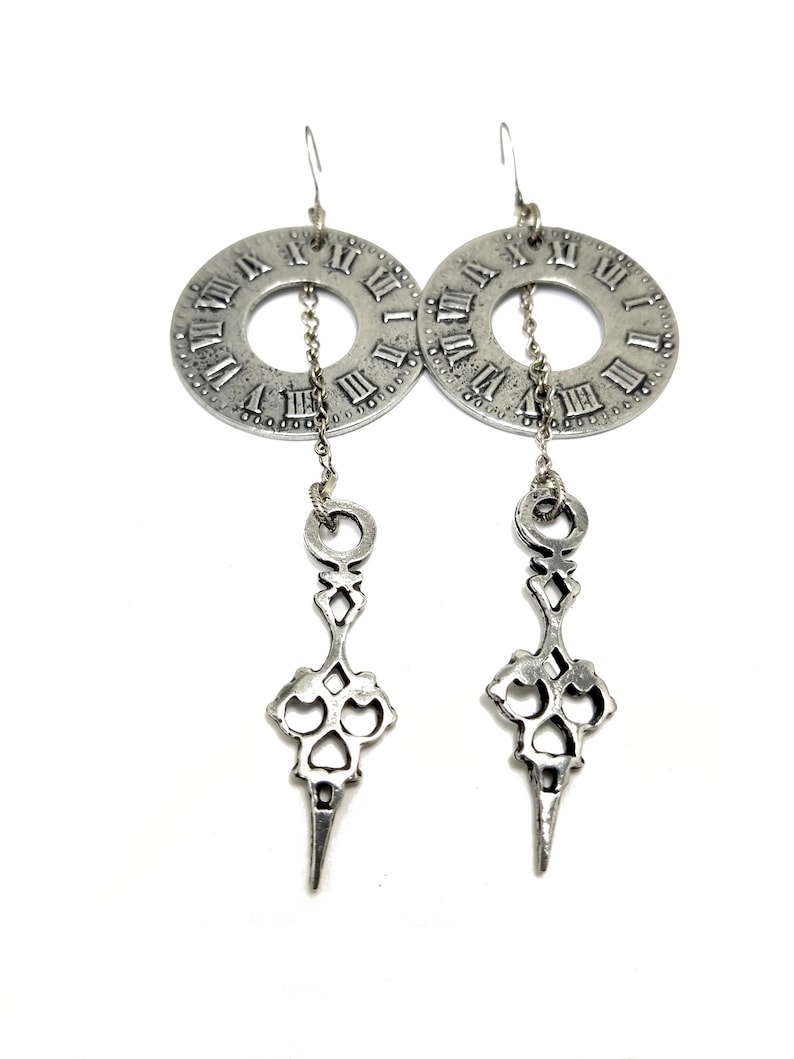 May include: Silver tone earrings with a clock face design and a dangling key-shaped charm.