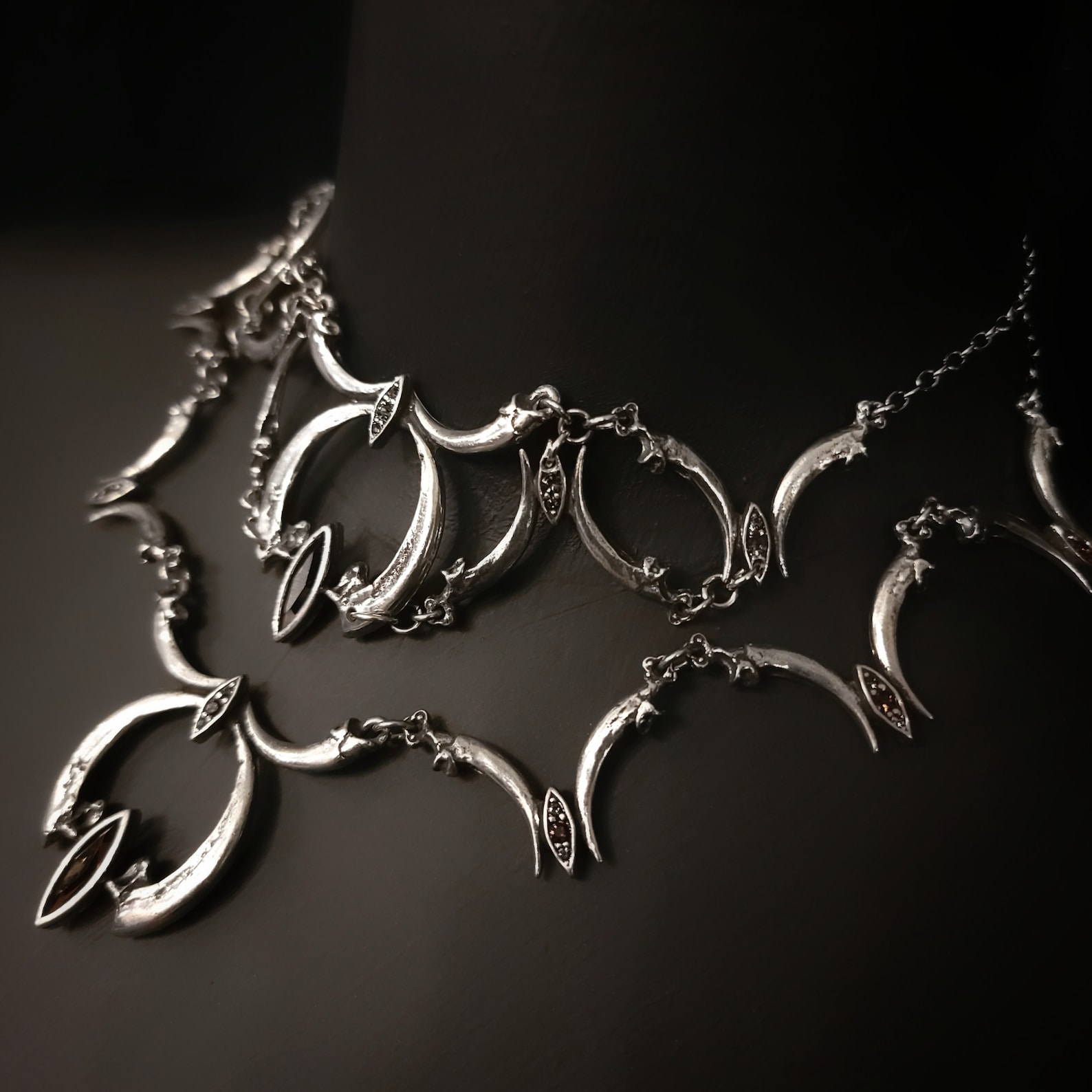 Close-up of silver bird claw goth necklace with double crescent and vintage crystals on dark mannequin.