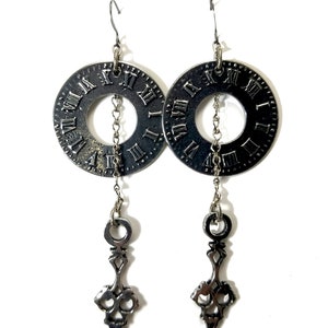 May include: Silver clock face earrings with a dangling clock hand design. The clock face has Roman numerals.