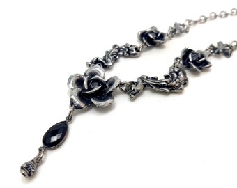 May include: A silver necklace with a black gemstone pendant and multiple rose-shaped charms. The necklace is made of a delicate chain and features intricate floral details.
