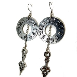 May include: Silver clock face earrings with a dangling ornate design. The clock face features Roman numerals.