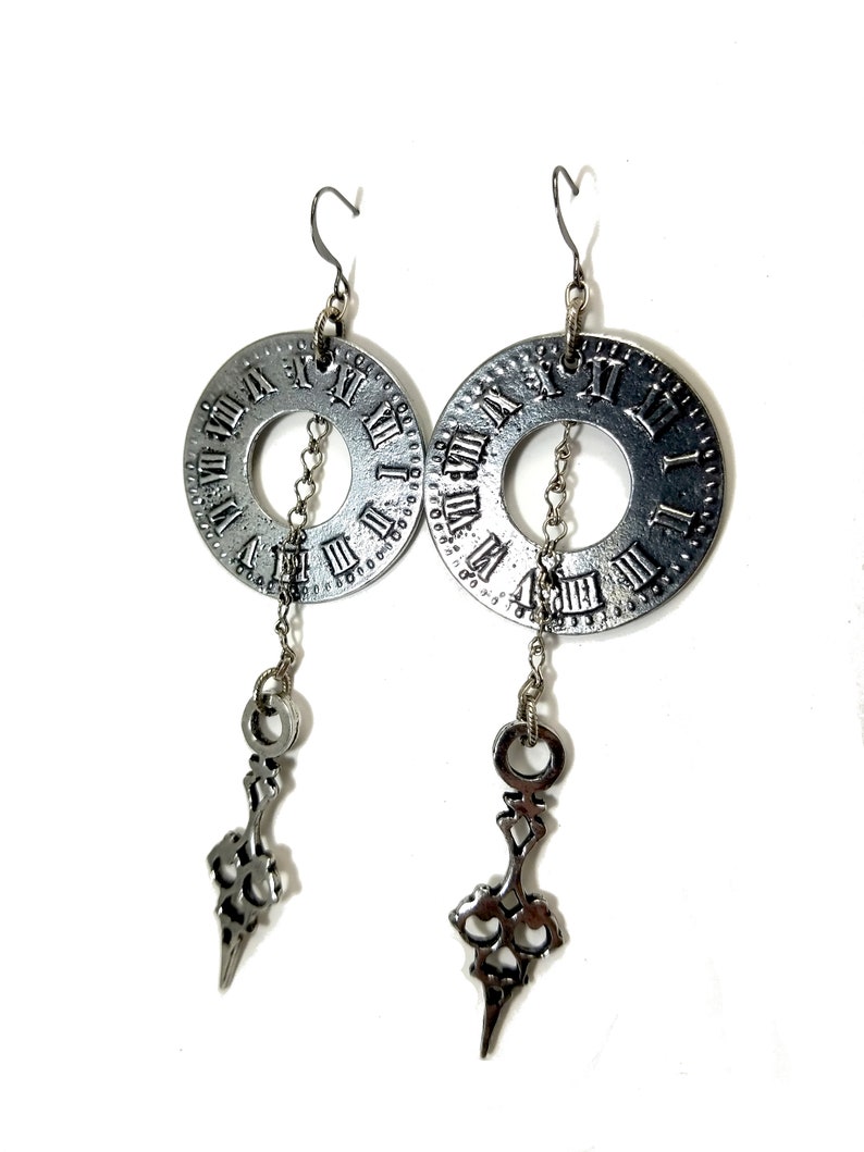 May include: Silver clock face earrings with a dangling ornate design. The clock face features Roman numerals.