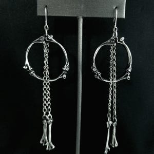 May include: A pair of silver earrings with a circular bone design and dangling bone charms.