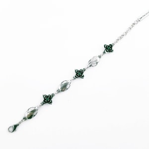 May include: Silver bracelet with a chain link design and four green flower charms. Each flower charm has a small green gemstone in the center.