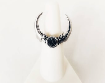 Puede incluir: Un anillo de plata con un diseño de media luna y una esfera de reloj negra en el centro.