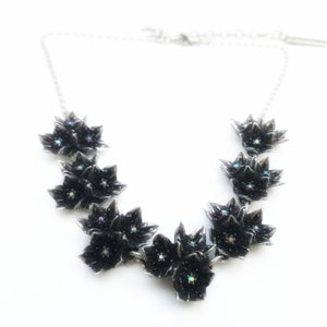 May include: A silver chain necklace with a cluster of black flower charms. Each flower has iridescent rhinestones in the center.