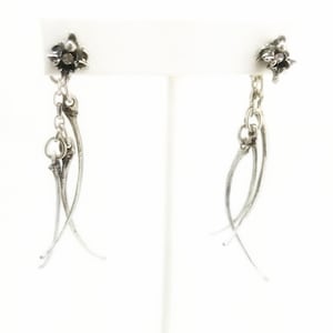 Puede incluir: Un par de pendientes de plata con un diseño de flor en la parte superior y una cadena colgante con dos piezas de plata curvas.