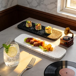 Puede incluir: Una escena de comedor con una fuente blanca texturizada con carne y patatas en rodajas, una tabla de servir de madera negra con aperitivos, un vaso de agua con limón y menta y un gramófono en miniatura.