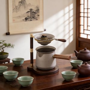 May include: A tea set featuring a metal teapot, a strainer, and several small green tea cups. The teapot has a wooden handle, and the strainer is suspended above it. The set is on a dark wooden table.