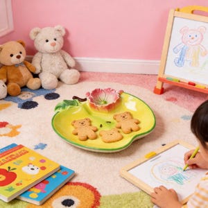 May include: A charming arrangement with a yellow apple-shaped serving dish, a pink floral bowl, and three bear-shaped biscuits. The scene includes teddy bears, children's books, and a small whiteboard with a drawing.
