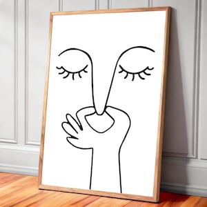 Könnte beinhalten: Abstrakter Kunstdruck mit Linien, der ein Gesicht mit geschlossenen Augen und einer Handgeste zeigt. Die schwarzen Linien befinden sich auf weißem Hintergrund und sind in einem hellbraunen Holzrahmen gerahmt. Das Kunstwerk lehnt an einer weißen Wand und einem Holzboden.